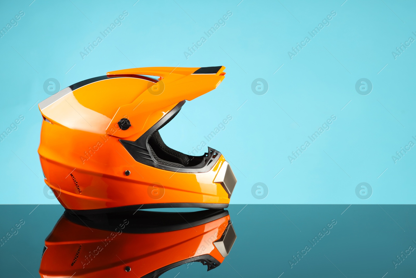 Photo of Modern motorcycle helmet with visor on mirror surface against light blue background. Space for text