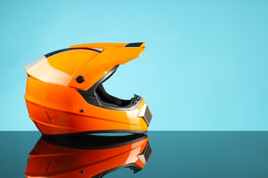 Photo of Modern motorcycle helmet with visor on mirror surface against light blue background. Space for text