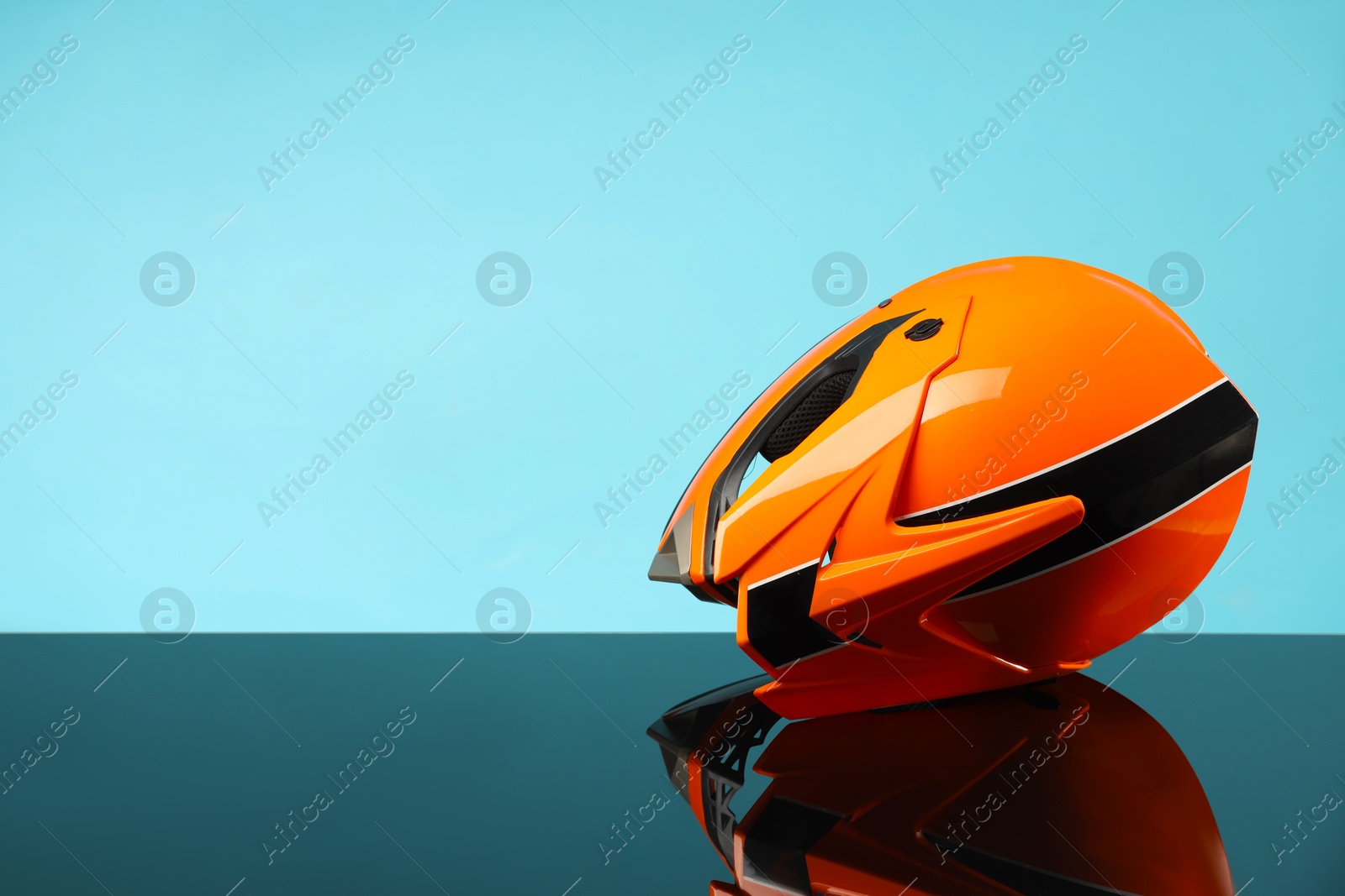 Photo of Modern motorcycle helmet with visor on mirror surface against light blue background. Space for text