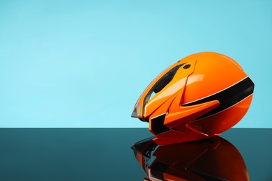 Photo of Modern motorcycle helmet with visor on mirror surface against light blue background. Space for text