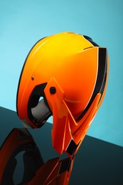 Photo of Modern motorcycle helmet with visor on mirror surface against light blue background