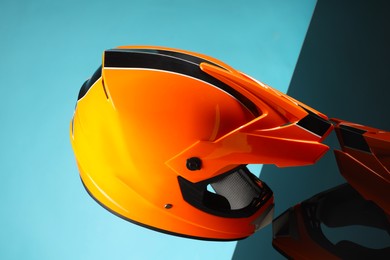 Photo of Modern motorcycle helmet with visor on mirror surface against light blue background