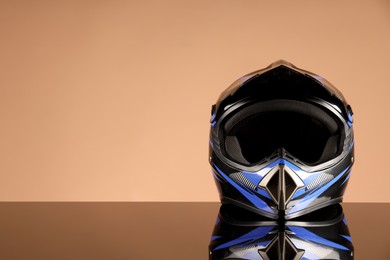 Photo of Modern motorcycle helmet with visor on mirror surface against beige background. Space for text