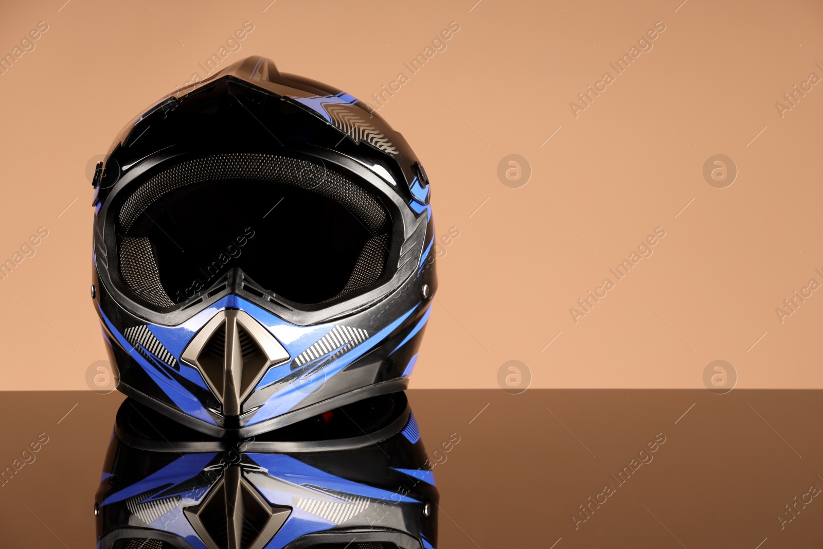 Photo of Modern motorcycle helmet with visor on mirror surface against beige background. Space for text