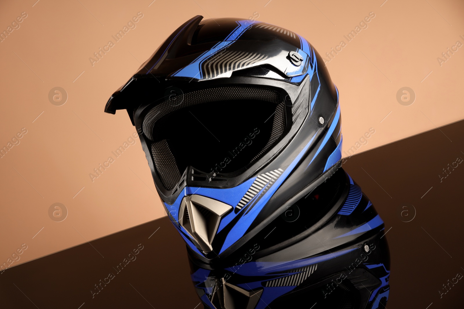 Photo of Modern motorcycle helmet with visor on mirror surface against beige background