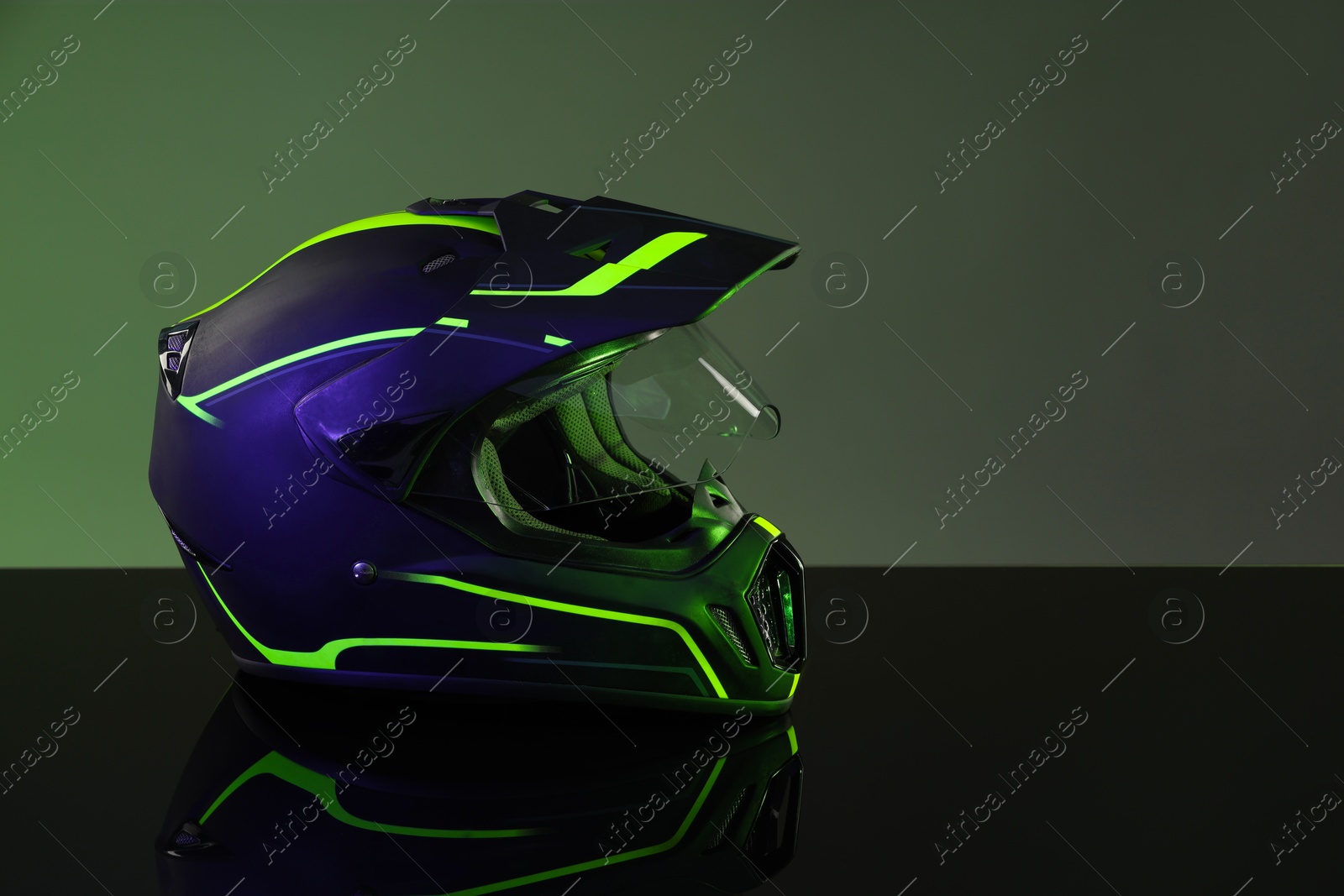 Photo of Modern motorcycle helmet with visor on mirror surface against grey background. Space for text