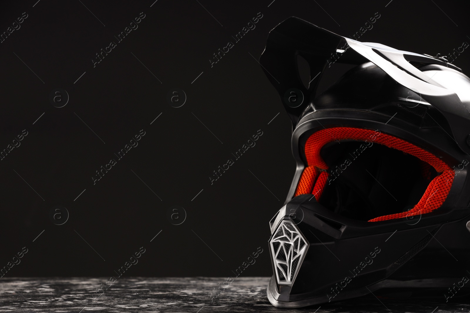 Photo of Modern motorcycle helmet with visor on grey stone surface against black background, closeup. Space for text