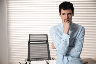 Photo of Embarrassed young man near table in office. Space for text