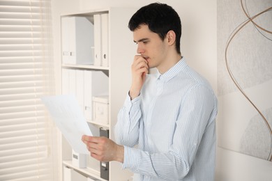 Photo of Embarrassed young man with document in office