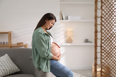 Photo of Beautiful pregnant woman sitting on sofa at home