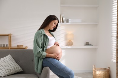 Photo of Beautiful pregnant woman sitting on sofa at home