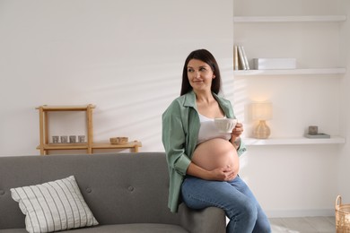 Beautiful pregnant woman sitting on sofa at home