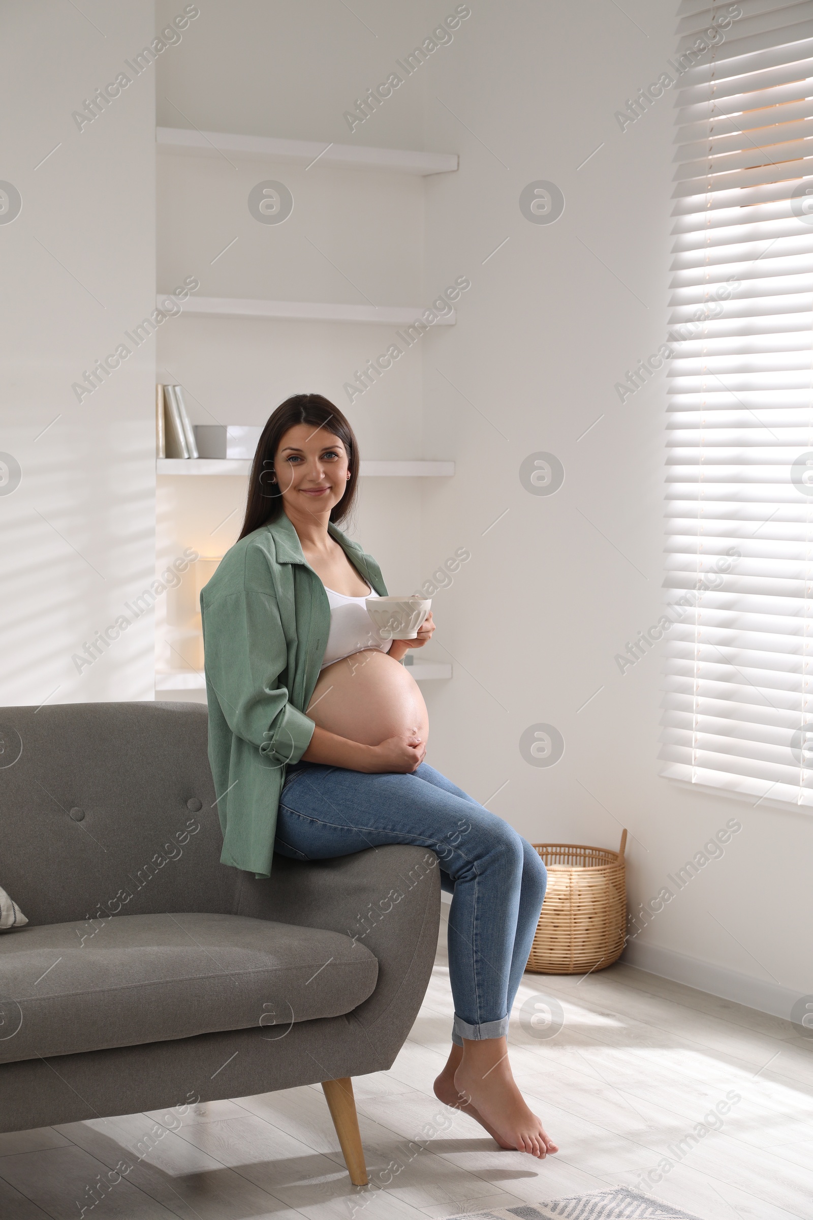 Photo of Beautiful pregnant woman sitting on sofa at home