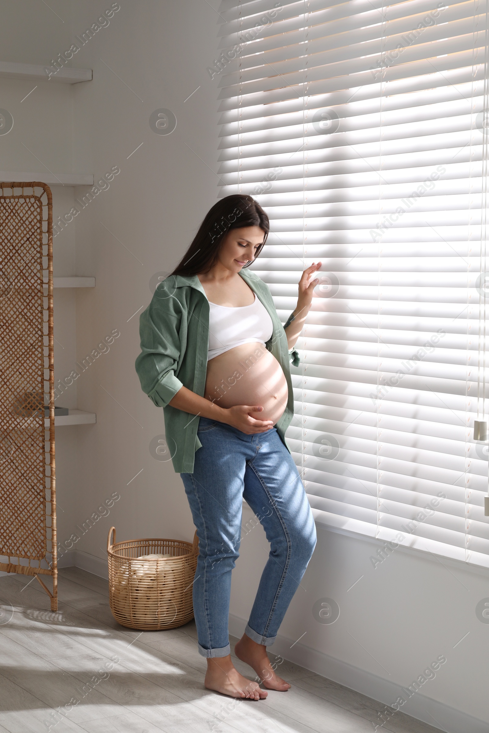 Photo of Beautiful pregnant woman near window blinds at home