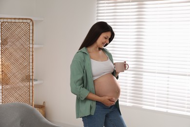 Beautiful pregnant woman with cup at home