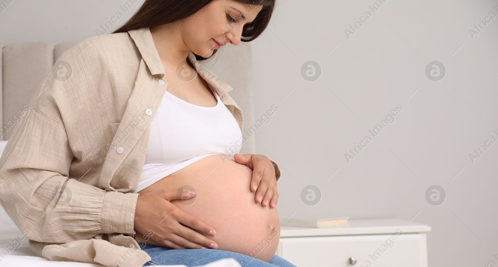 Photo of Beautiful pregnant woman on bed at home, space for text