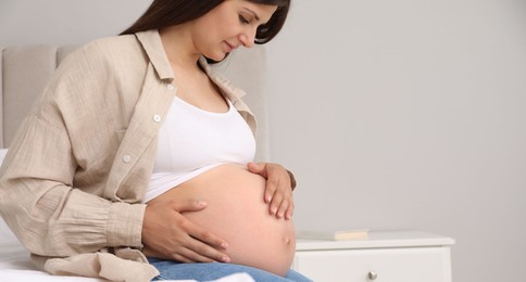 Beautiful pregnant woman on bed at home, space for text