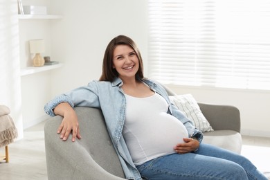 Beautiful pregnant woman sitting on sofa at home