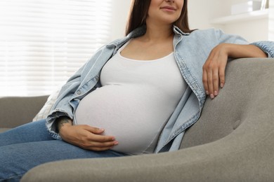 Beautiful pregnant woman sitting on sofa at home