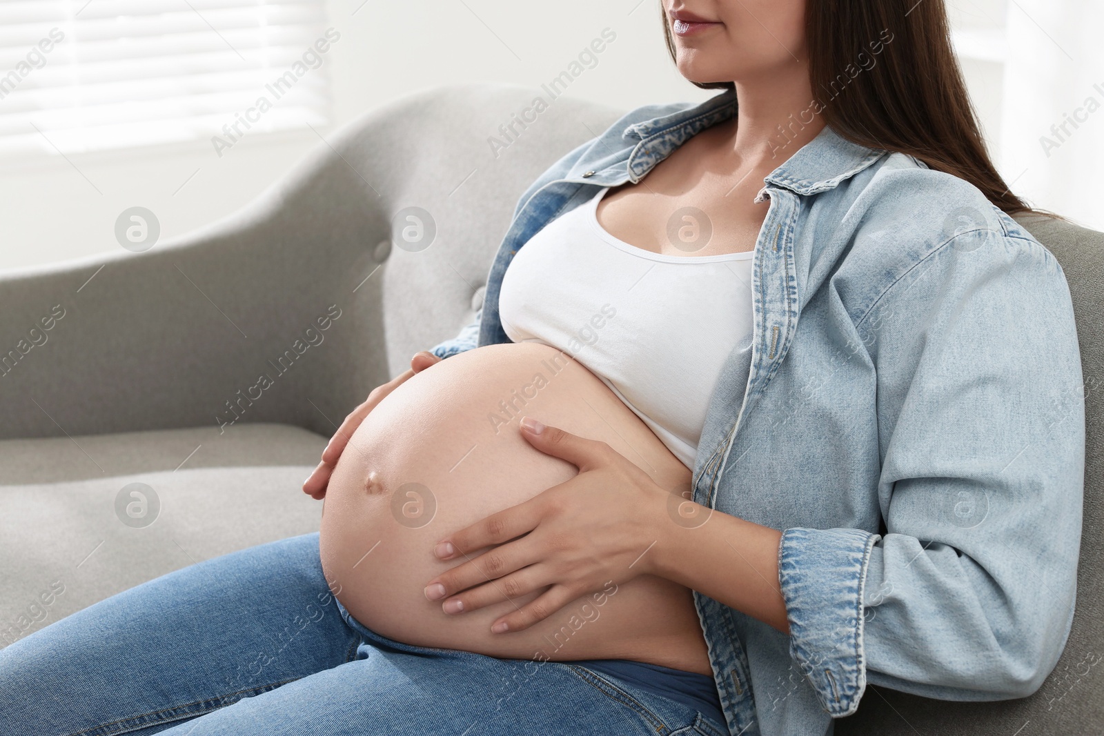 Photo of Pregnant woman sitting on sofa at home, closeup