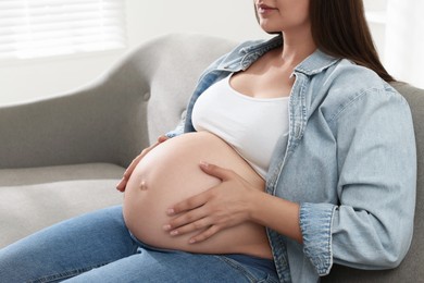 Pregnant woman sitting on sofa at home, closeup