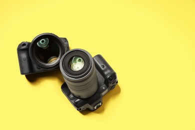 Photo of Two modern photo cameras on yellow background, above view. Space for text