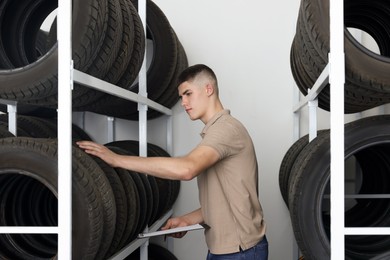 Photo of Young man with clipboard near car tires in auto store