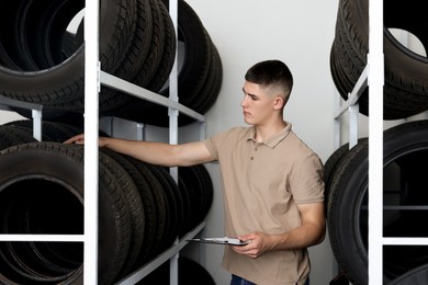 Photo of Young man with clipboard near car tires in auto store