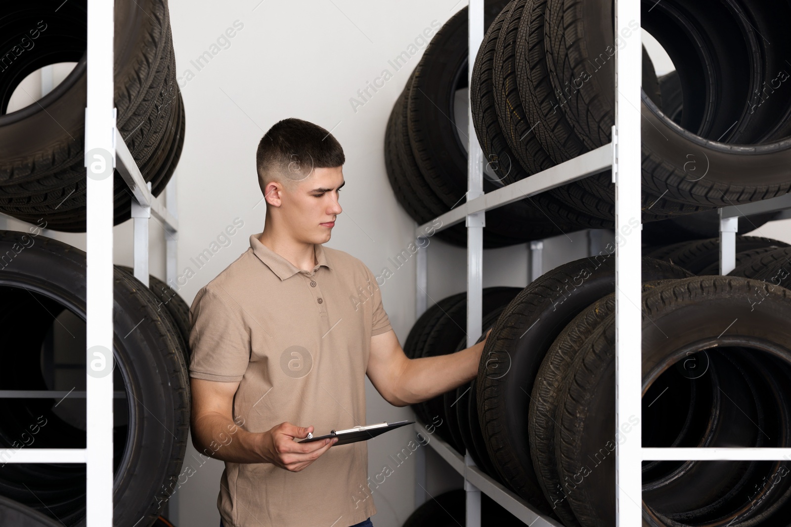 Photo of Young man with clipboard near car tires in auto store