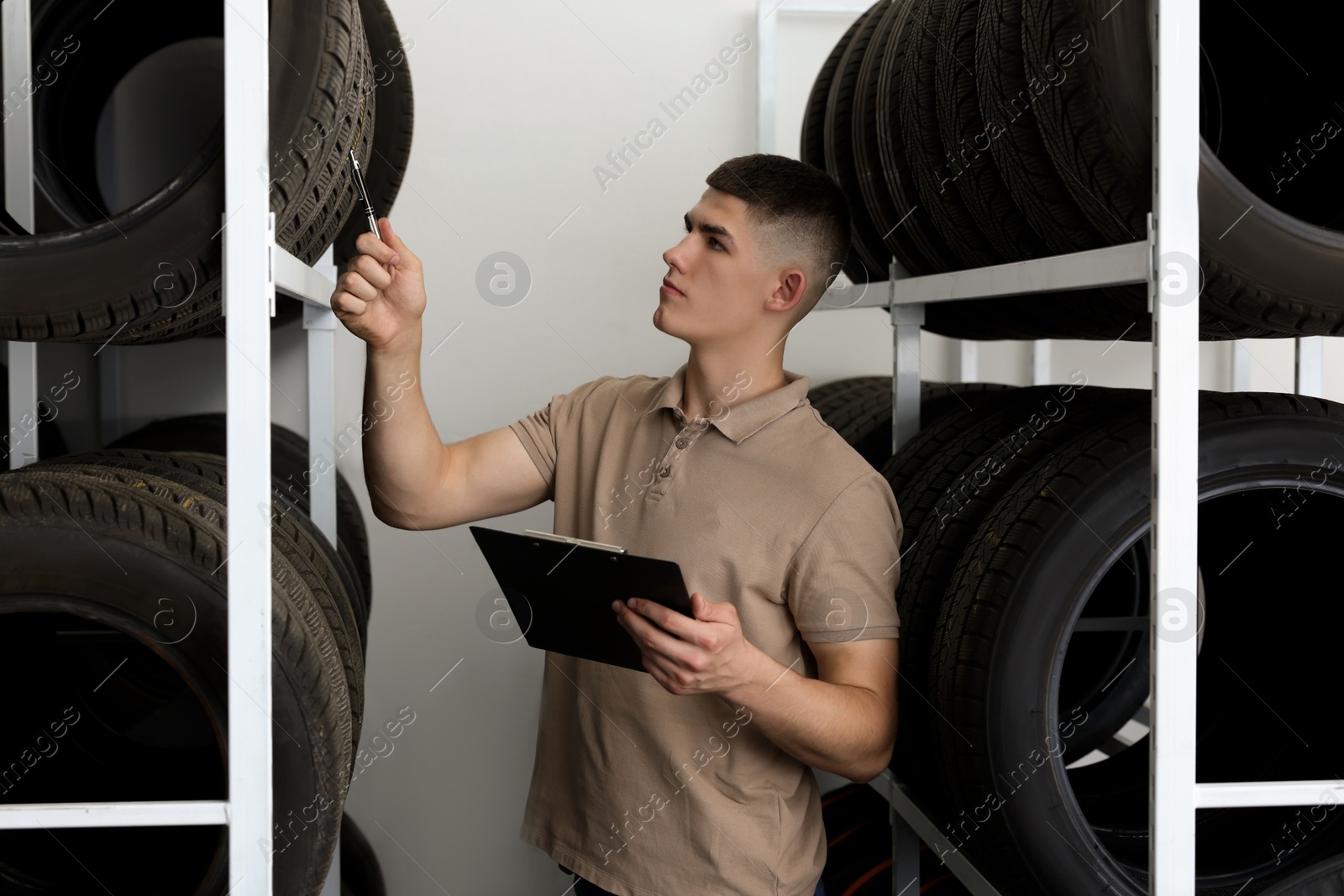 Photo of Young man with clipboard near car tires in auto store