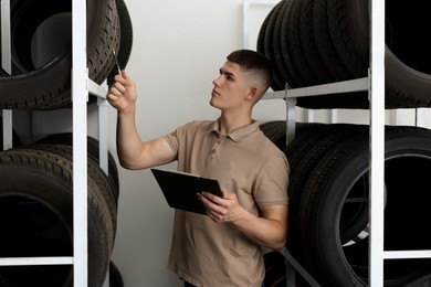 Young man with clipboard near car tires in auto store