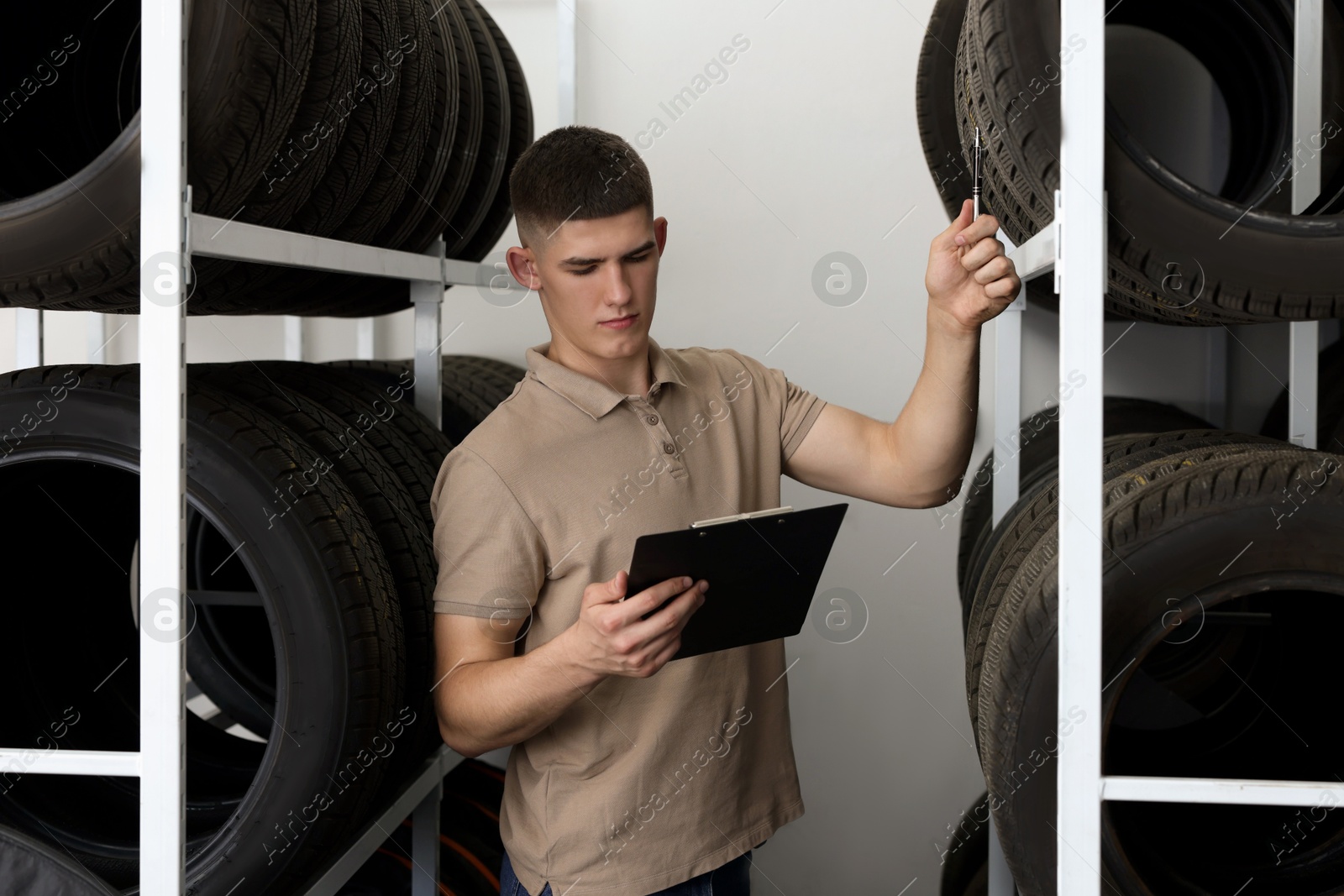 Photo of Young man with clipboard near car tires in auto store