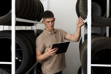 Photo of Young man with clipboard near car tires in auto store