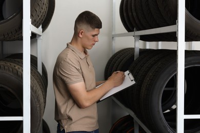 Photo of Young man with clipboard taking notes near car tires in auto store