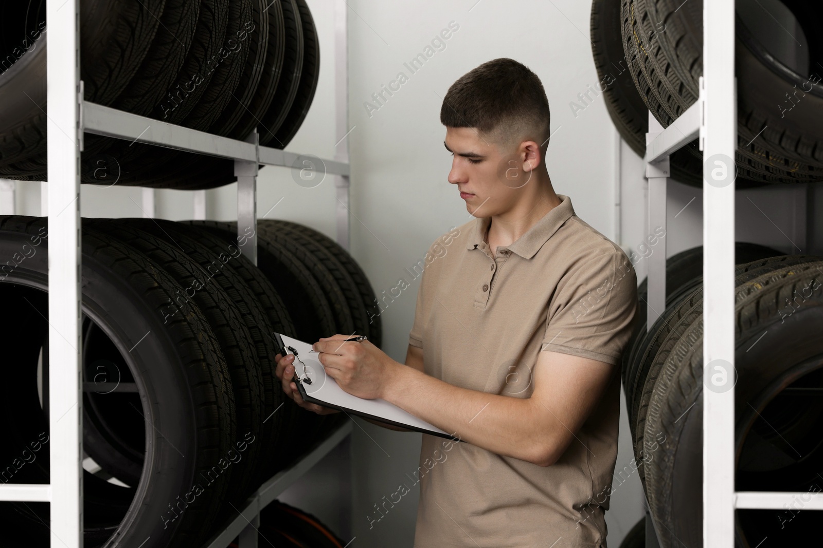 Photo of Young man with clipboard taking notes near car tires in auto store