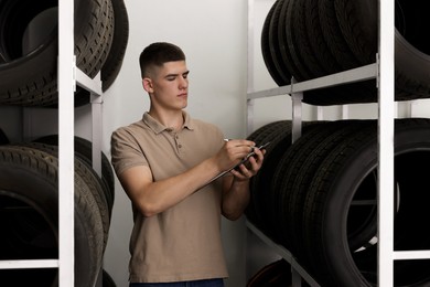 Young man with clipboard taking notes near car tires in auto store