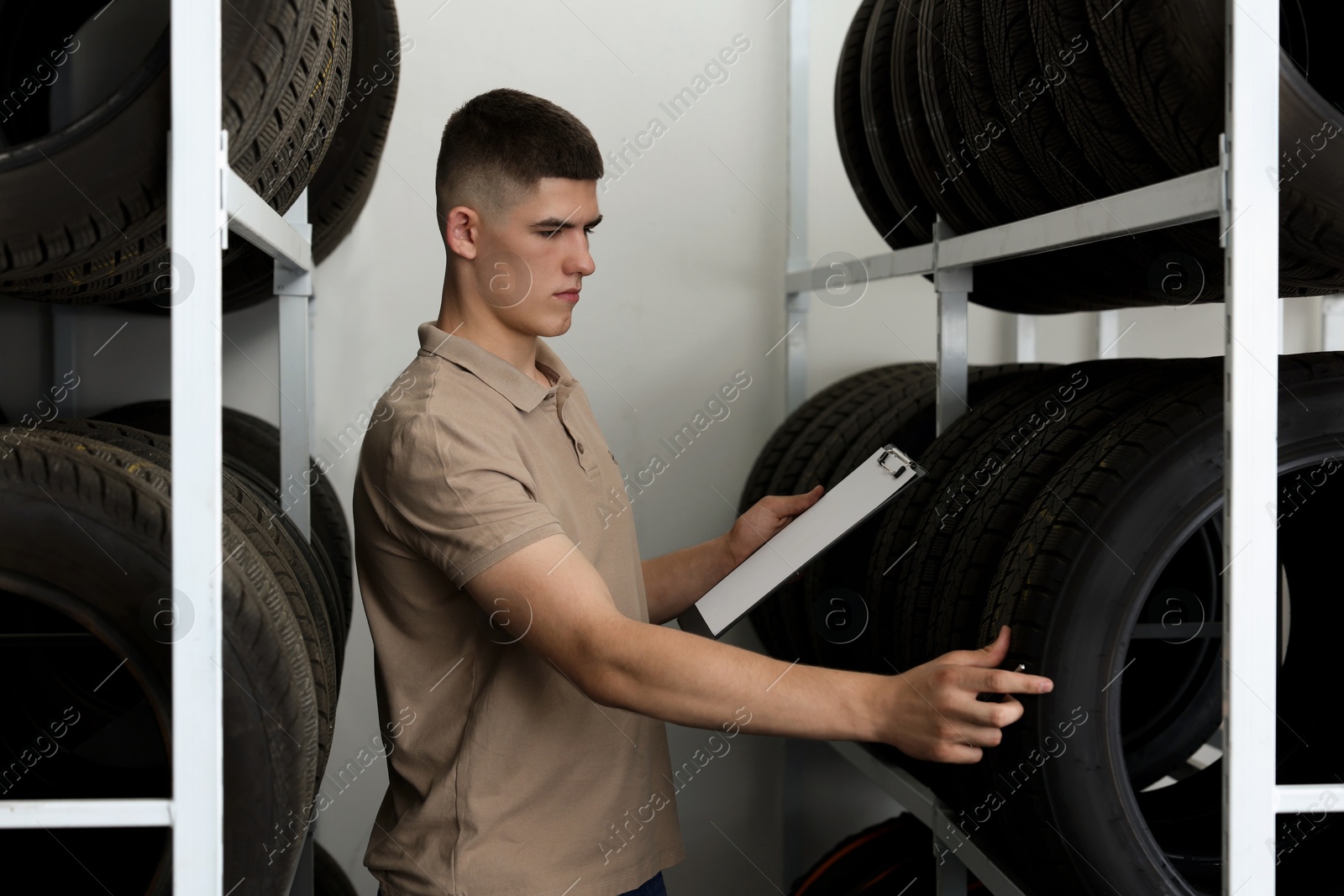 Photo of Young man with clipboard near car tires in auto store