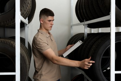 Young man with clipboard near car tires in auto store