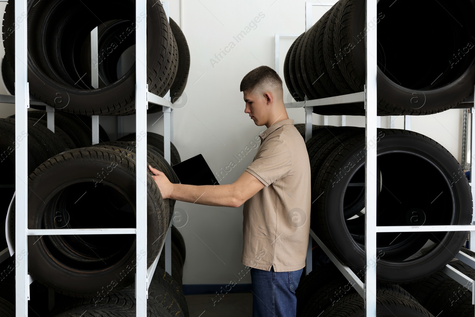 Photo of Young man with clipboard near car tires in auto store