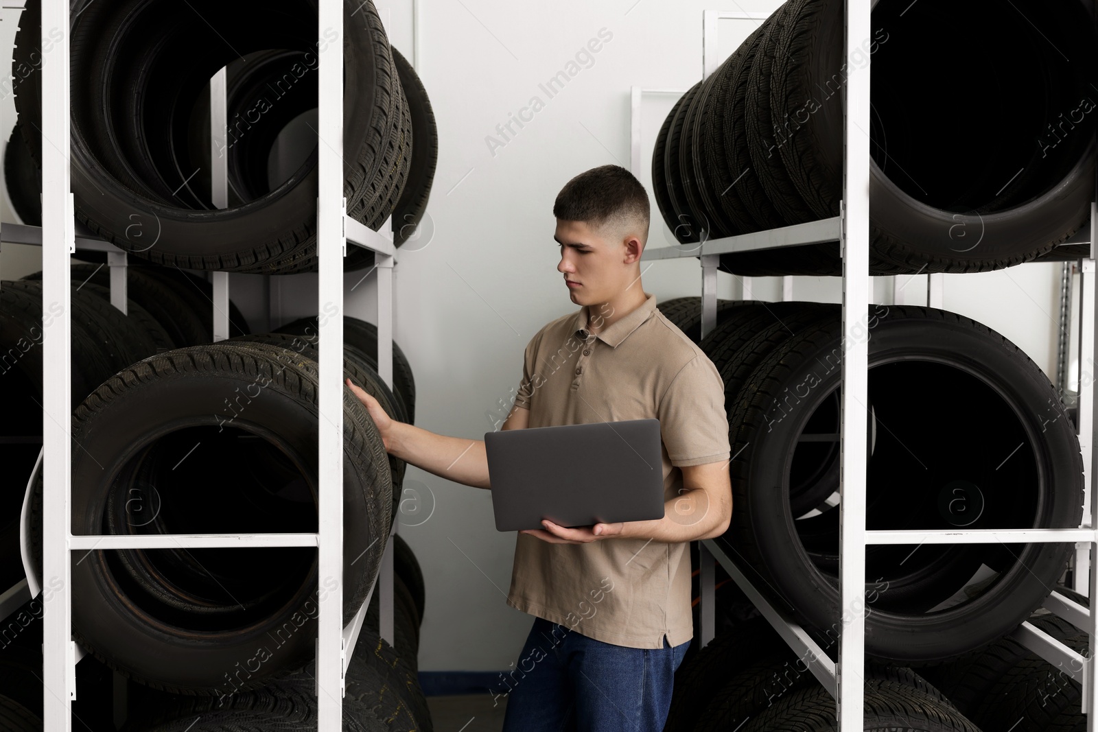 Photo of Young man with laptop near car tires in auto store