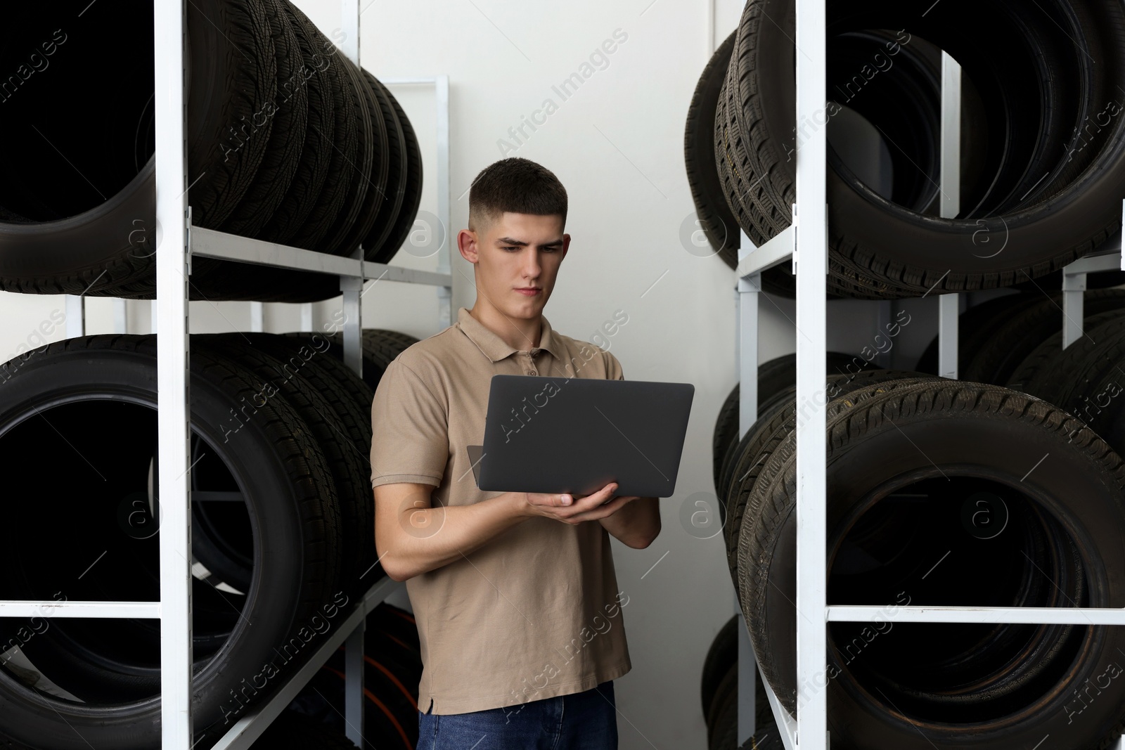 Photo of Young man with laptop near car tires in auto store