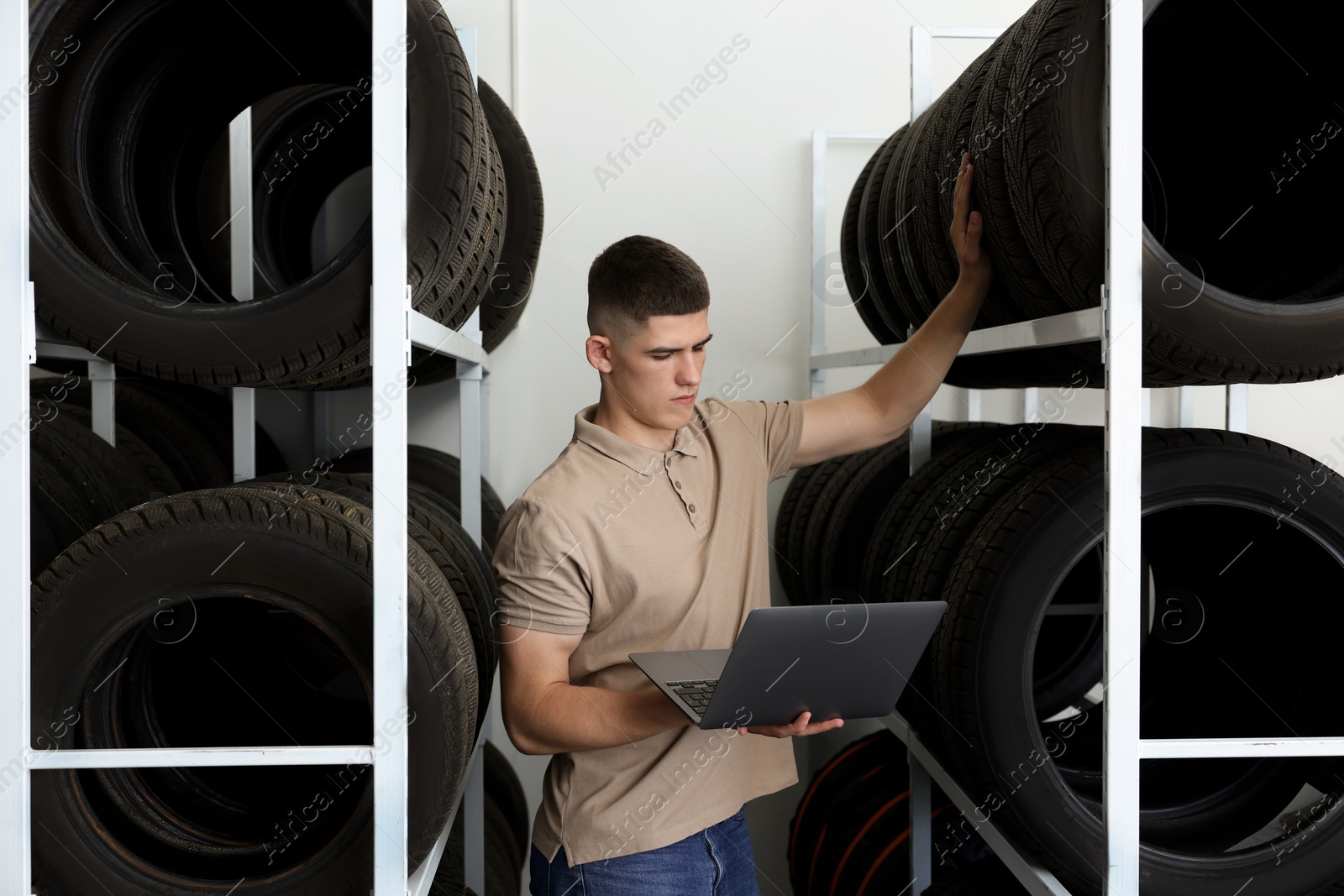 Photo of Young man with laptop near car tires in auto store