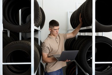 Photo of Young man with laptop near car tires in auto store