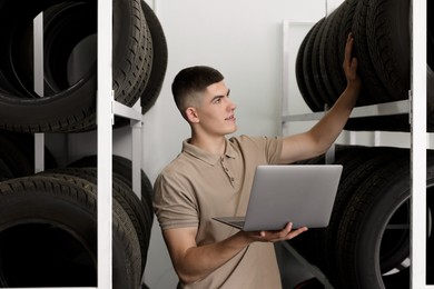 Photo of Young man with laptop near car tires in auto store