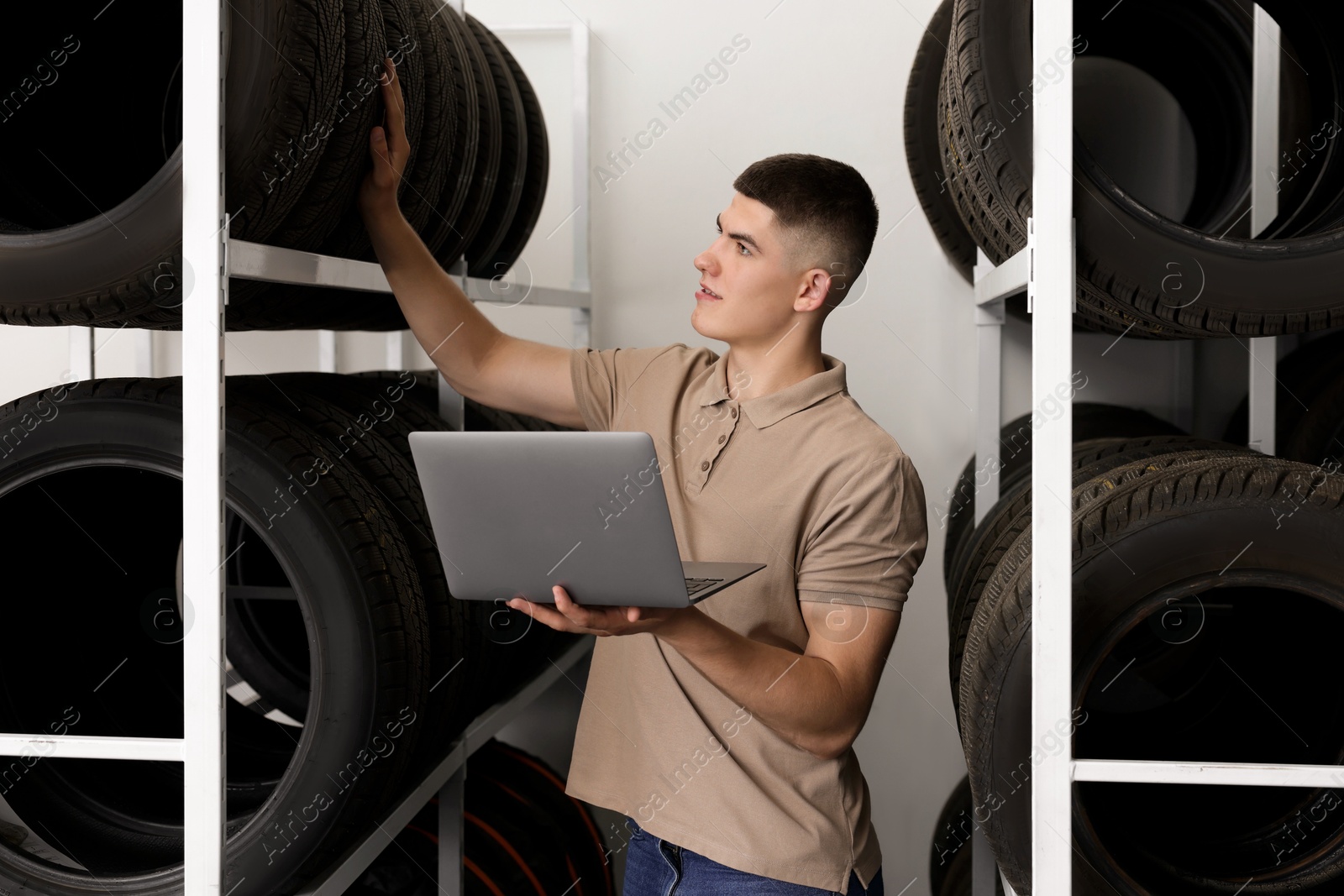 Photo of Young man with laptop near car tires in auto store