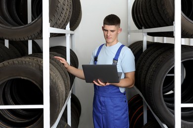 Young man with laptop near car tires in auto store