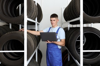 Photo of Young man with laptop near car tires in auto store