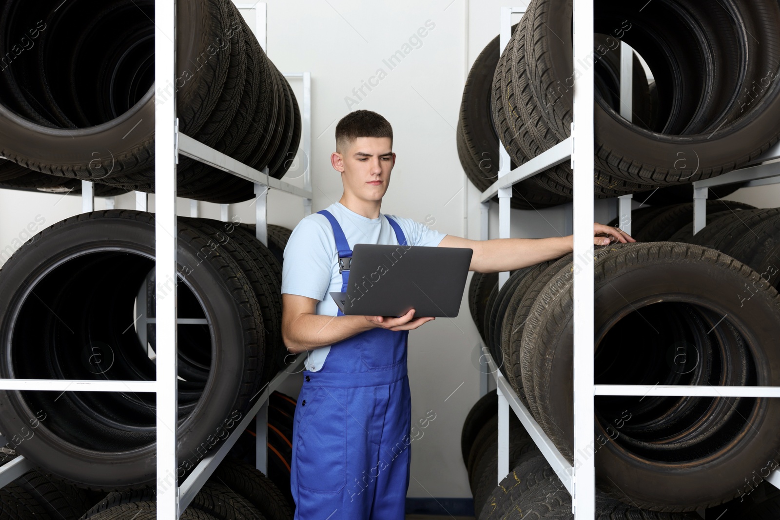 Photo of Young man with laptop near car tires in auto store