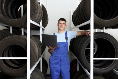 Smiling young man with laptop near car tires in auto store