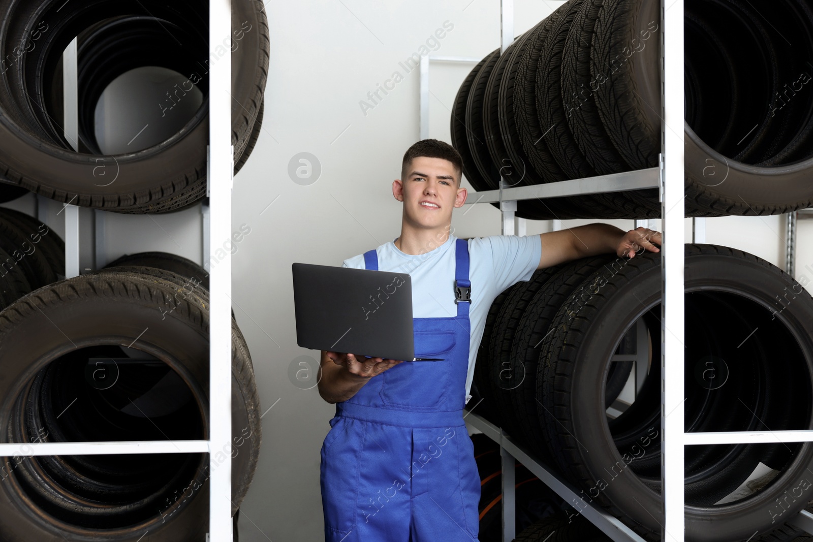 Photo of Smiling young man with laptop near car tires in auto store